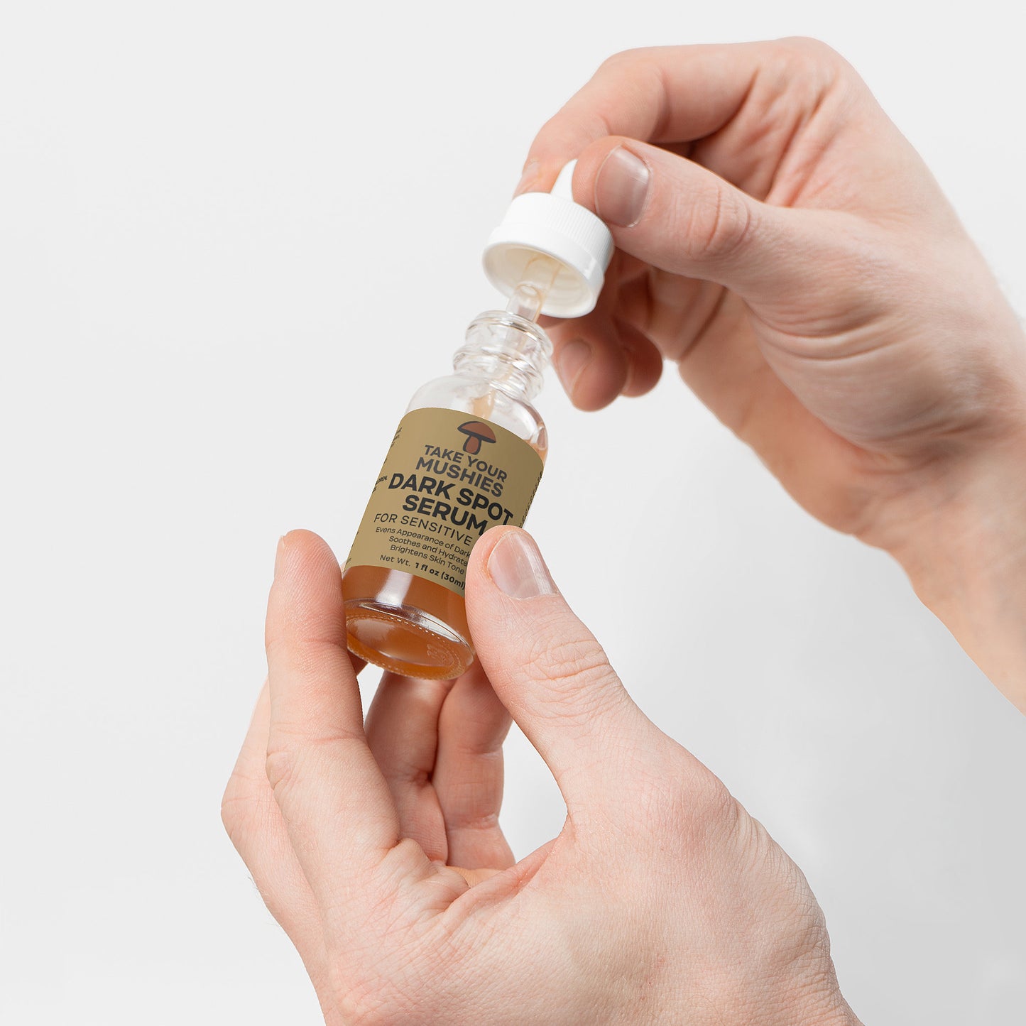 Hand holding a small bottle of dark spot serum with a dropper against a light background. Takeyourmushies