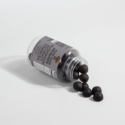 Bottle of supplements with black capsules spilling out on a light gray background